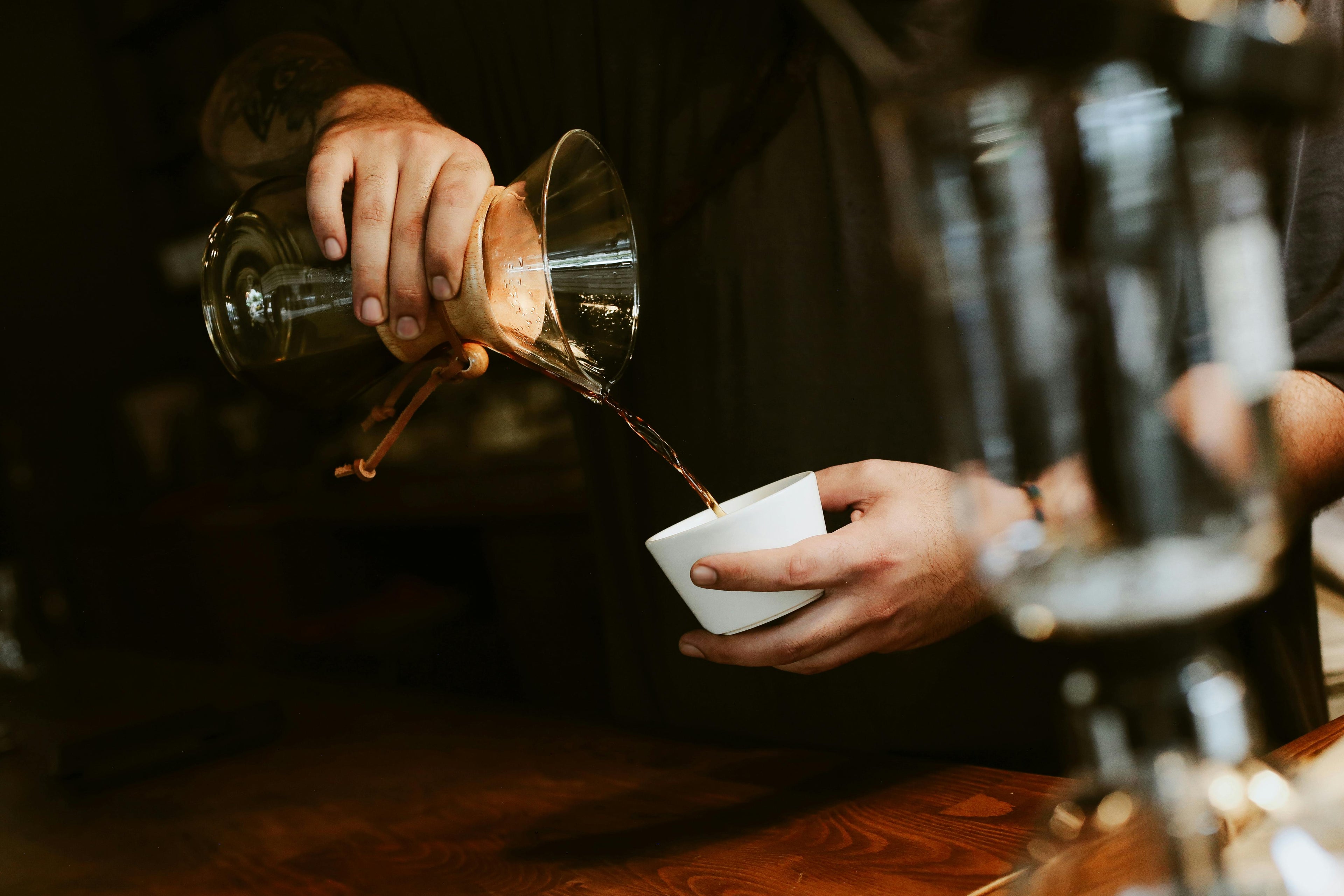 Barista pouring coffee from a glass portafilter into a white cup.